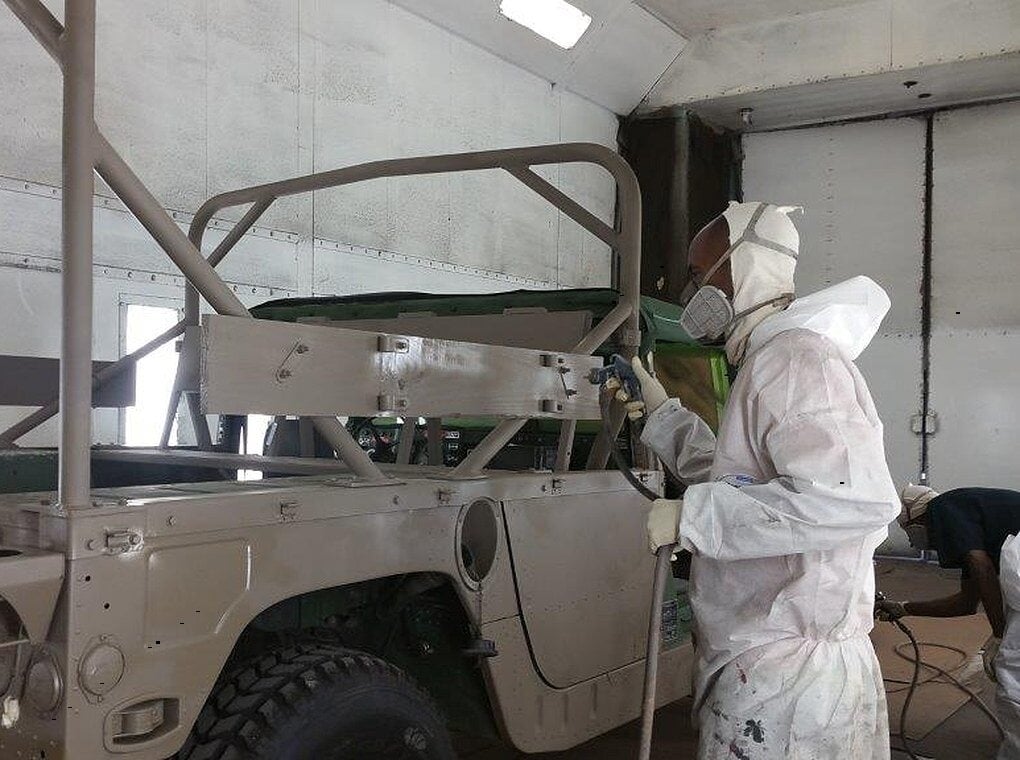 worker wearing PPE painting tactical vehicle with paint gun